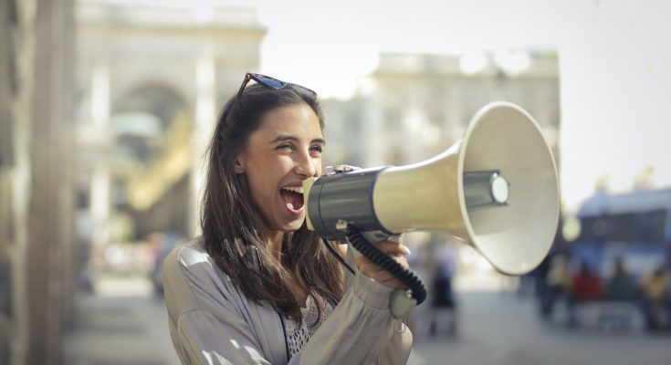 cheerful young woman screaming into megaphone